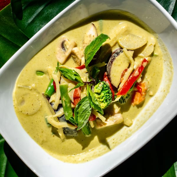 Thailicious green curry with mushrooms, bamboo shoots, bell peppers, broccoli, and basil in a white bowl.