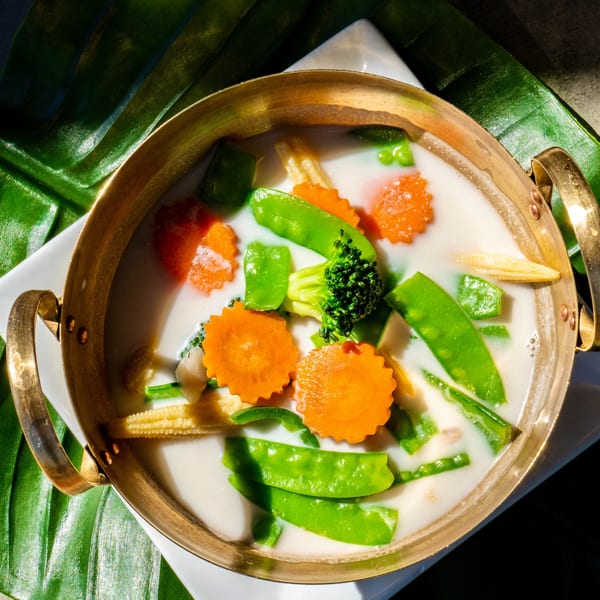 Thailicious' Tom Kha soup with carrots, broccoli, snow peas, and baby corn in a brass pot.