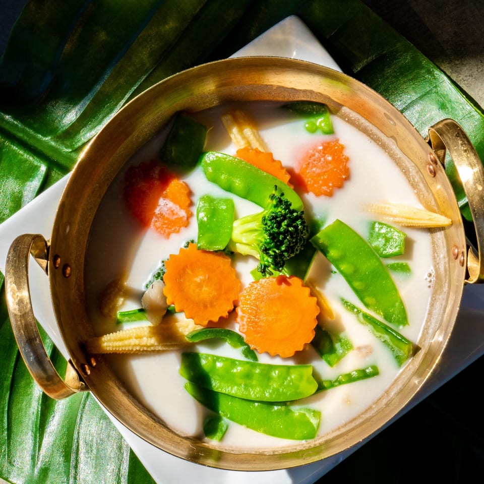 Thailicious' Tom Kha soup with carrots, broccoli, snow peas, and baby corn in a brass pot.