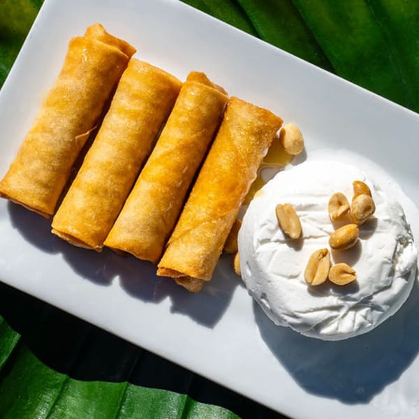 Four golden fried banana spring rolls with a scoop of coconut ice cream topped with peanuts.