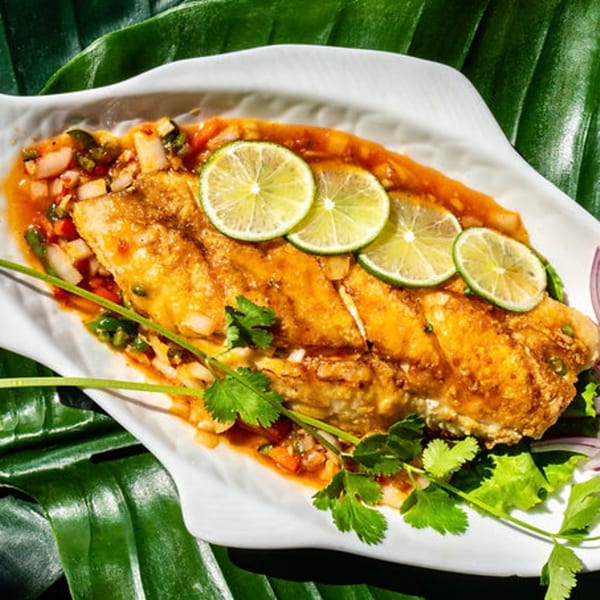 Thailicious' whole fried fish, garnished with lime slices, cilantro, and chili sauce.
