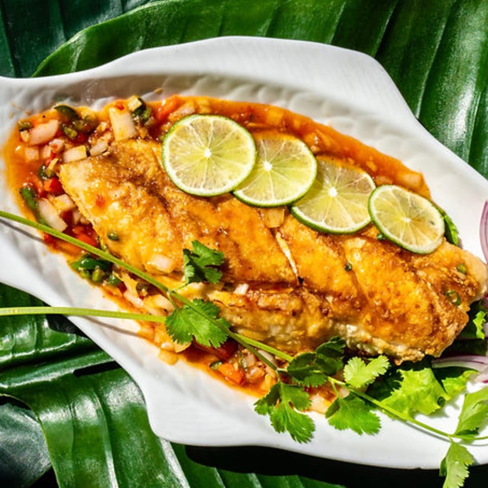 Thailicious' whole fried fish, garnished with lime slices, cilantro, and chili sauce.