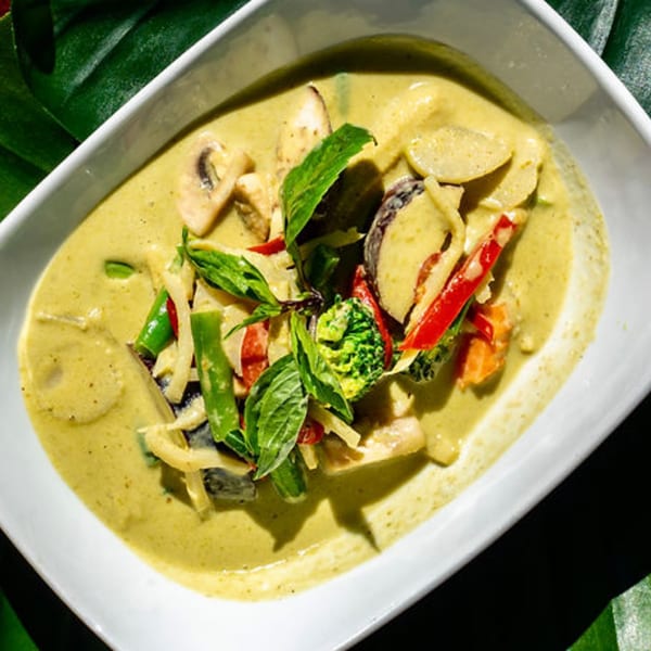 Thailicious green curry with mushrooms, bamboo shoots, bell peppers, broccoli, and basil in a white bowl.