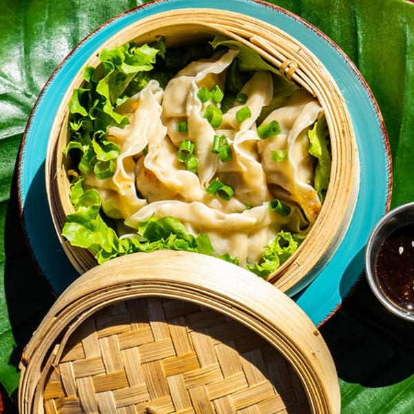 Steamed dumplings with green onions and lettuce in a bamboo steamer, with a side of sauce.
