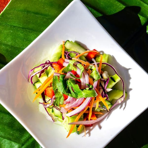 A vibrant Thai salad with cucumbers, carrots, red onions, and cilantro in a white square bowl.