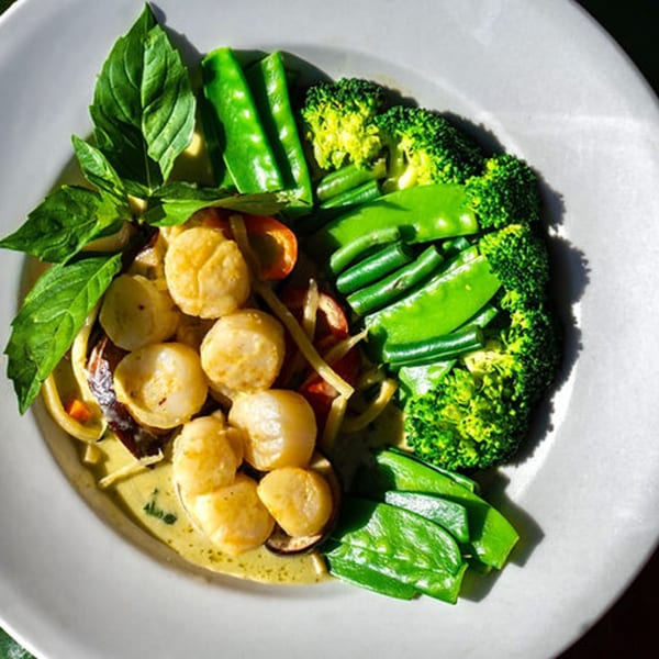 Thailicious Thai green curry with scallops, broccoli, snap peas, and basil on a white plate.