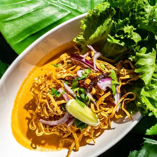 Thailicious' Khao Soi, a Thai noodle dish with curry, lime, red onion, and lettuce.