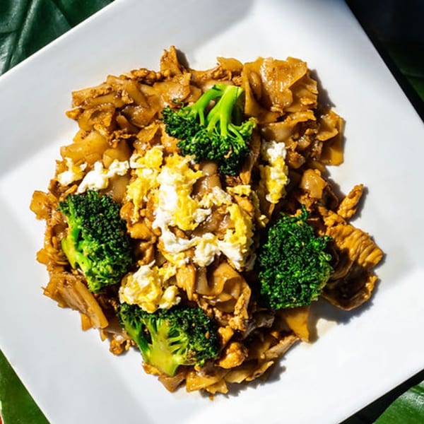 Thailicious' Pad See Ew with wide noodles, scrambled egg, broccoli, and chicken on a white plate.