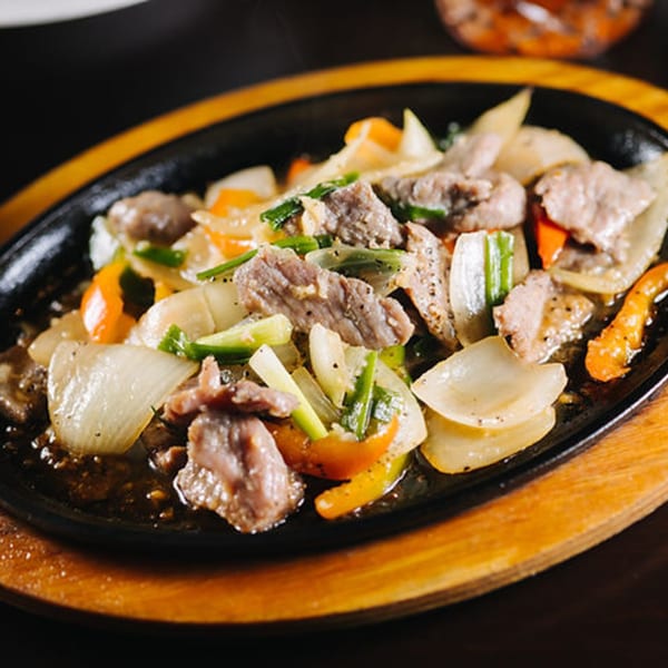 Sizzling Thai beef with onions, bell peppers, and green onions on a black platter.