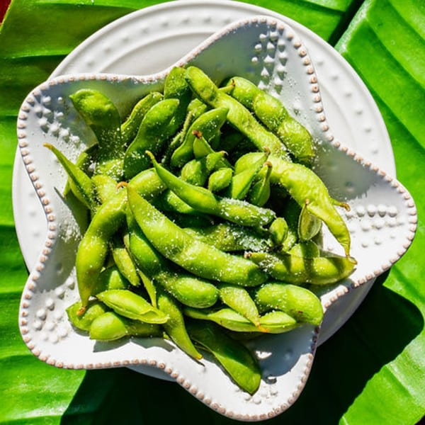 A white star-shaped bowl filled with salted edamame pods, set on a green banana leaf.