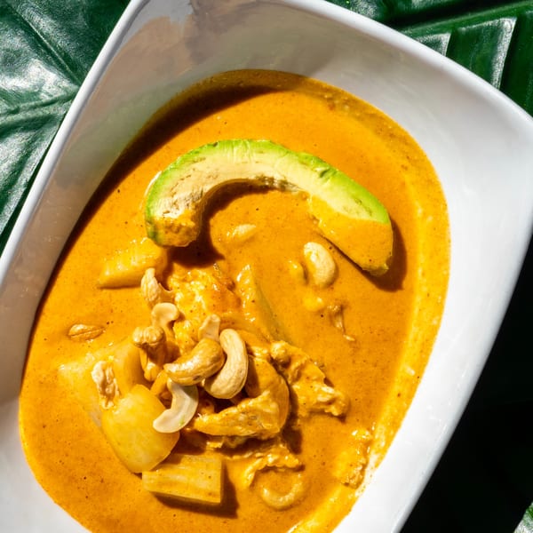 Thailicious yellow curry with chicken, cashews, and avocado in a white bowl on a green leaf.