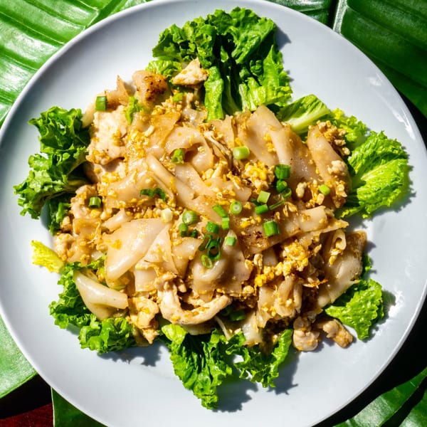 Thailicious' Pad See Ew, a Thai dish with wide noodles, chicken, egg, and green onions on lettuce.