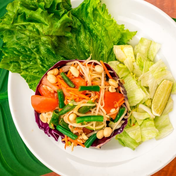 Thailicious papaya salad with green beans, tomatoes, peanuts, and lime on a white plate.