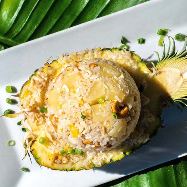 Thailicious pineapple fried rice, served in a pineapple half, garnished with green onions.