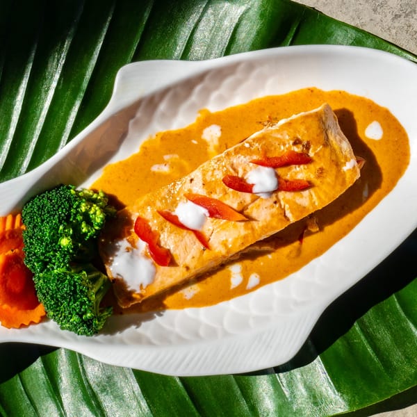 Thailicious salmon in red curry sauce with broccoli and carrots on a fish-shaped plate.