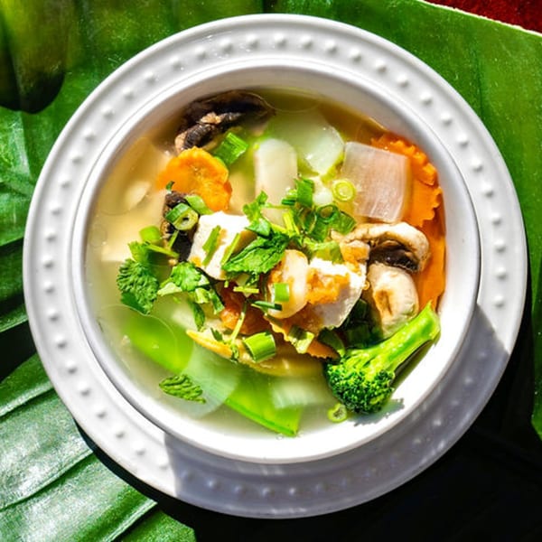 Thailicious clear soup with chicken, mushrooms, carrots, broccoli, and herbs in a white bowl.