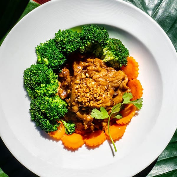 Thailicious garlic pork with broccoli, carrots, and cilantro on a white plate.