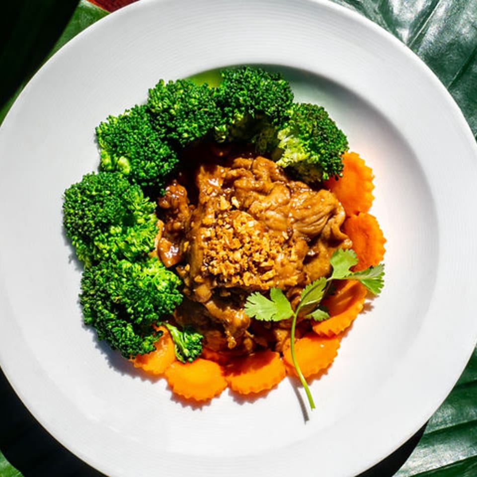 Thailicious garlic pork with broccoli, carrots, and cilantro on a white plate.