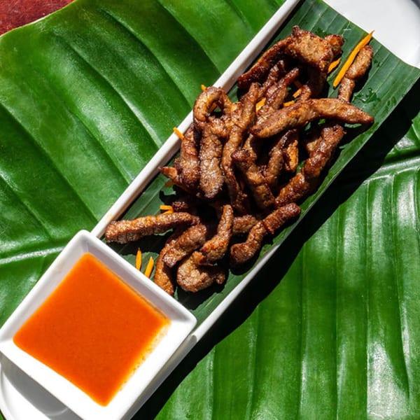Thailicious' fried Thai beef jerky with a side of chili sauce, served on a banana leaf.